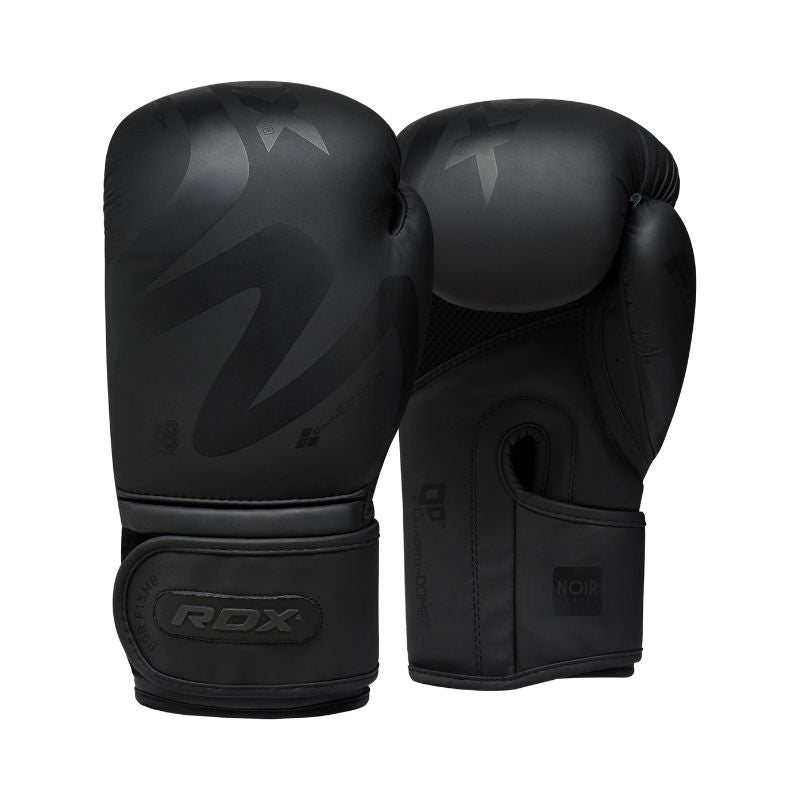 A pair of black boxing gloves with a matte finish and subtle patterns, featuring the RDX logo on the wrist straps. One glove stands upright while the other is tilted to show the palm side.