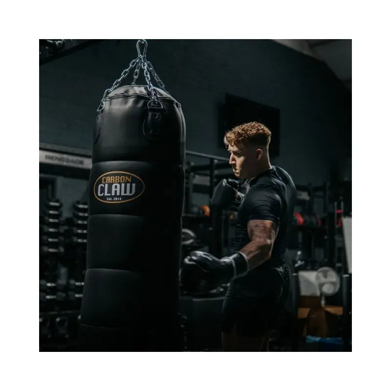 The Carbon Claw Pro FX-7 Series 4FT Heavy Punch Bag (45kg, foam padded) in black synthetic leather with chain attachments and logo is designed for boxing training, shown hanging against a plain white background.
