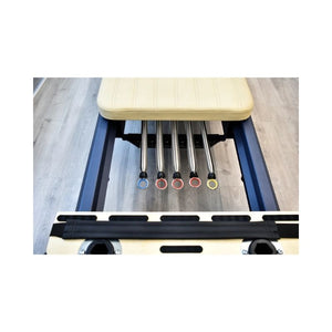 Close-up of a Pilates reformer with five HEGREN Reformer Springs – Colour-Coded Resistance Options by Hegren, each tipped with a colored ring, beneath a padded beige carriage—showcasing premium quality Pilates accessories.
