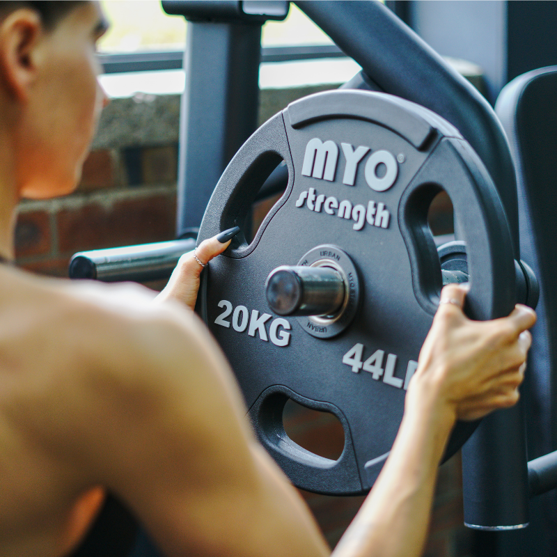 Person holding a weight plate with 'MYO strength' branding in a gym setting