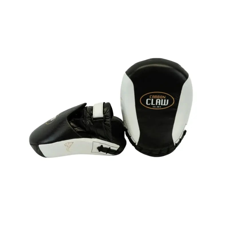 A pair of CARBON CLAW Pro FX-7 Series Curved Catch Pads—the genuine leather boxing coaching mitts—shown in black and white: one lies flat to display the logo, while the other is tilted to show the hand slot and strap.