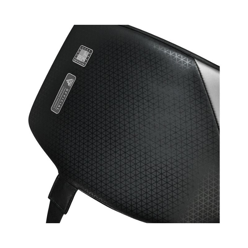 Close-up of a black textured surface with a subtle triangular pattern, featuring a small square chip and a rectangular label with text, and a strap attached at the bottom.