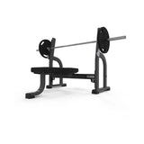 The JORDAN Olympic Flat Bench by Jordan is a black and gray UK-built commercial weight bench with a barbell and weights, ideal for upper-body strength training and Olympic Flat Bench press exercises, shown on a white background.