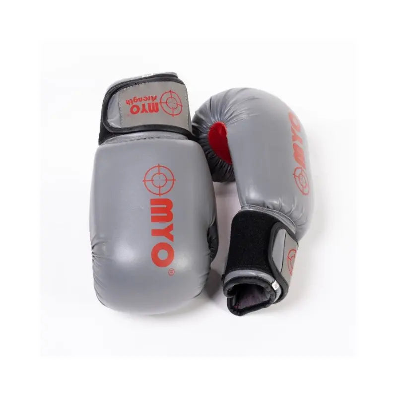 A pair of MYO Strength Leather Boxing Gloves – Grey/Red (12oz, 14oz, 16oz) are displayed on a white surface—one upright and one on its side—showcasing quality design and wrist support for sparring.