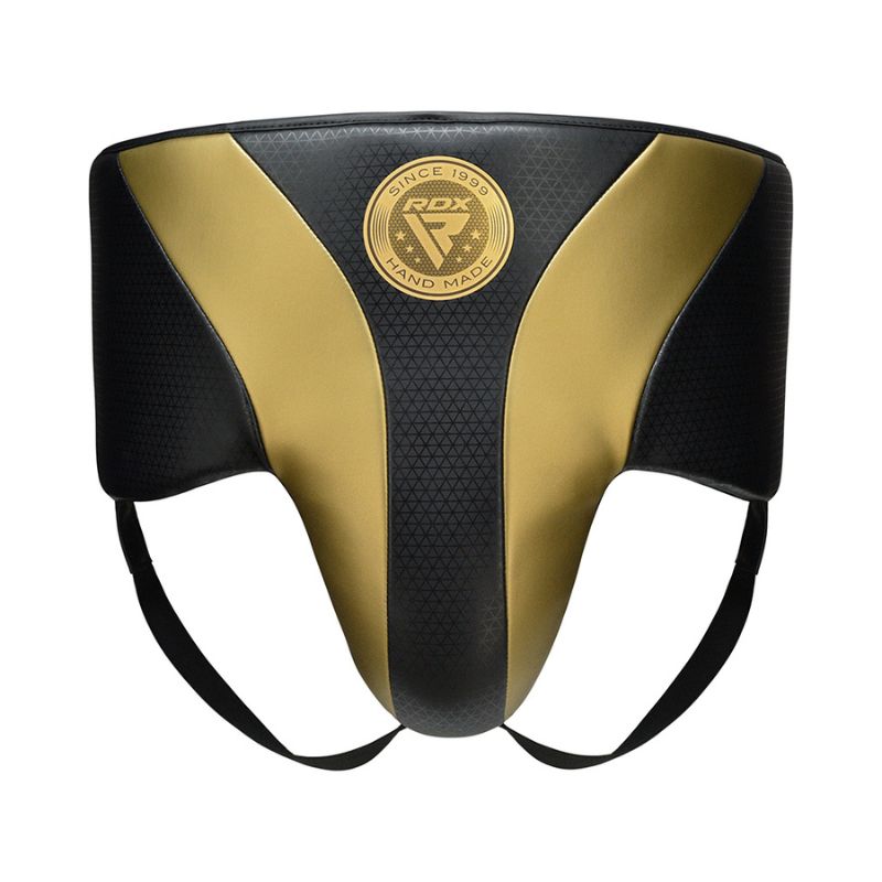 A black and gold protective groin guard with a circular "RDX Hand Made" logo in the center, featuring two waistband straps and a padded front design.