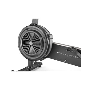 Close-up of a black rowing machine, showing the circular fan flywheel and part of the frame with the words "HALF HUMAN" printed on it.