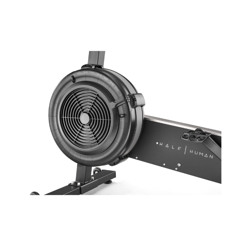Close-up of a black rowing machine, showing the circular fan flywheel and part of the frame with the words "HALF HUMAN" printed on it.