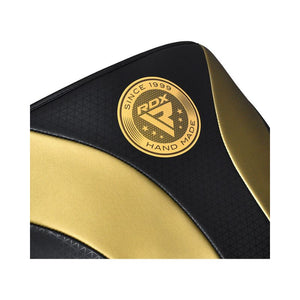 Close-up of a black and gold padded surface with the "RDX Hand Made Since 1999" logo printed on it. The design features curved lines and textured patterns.