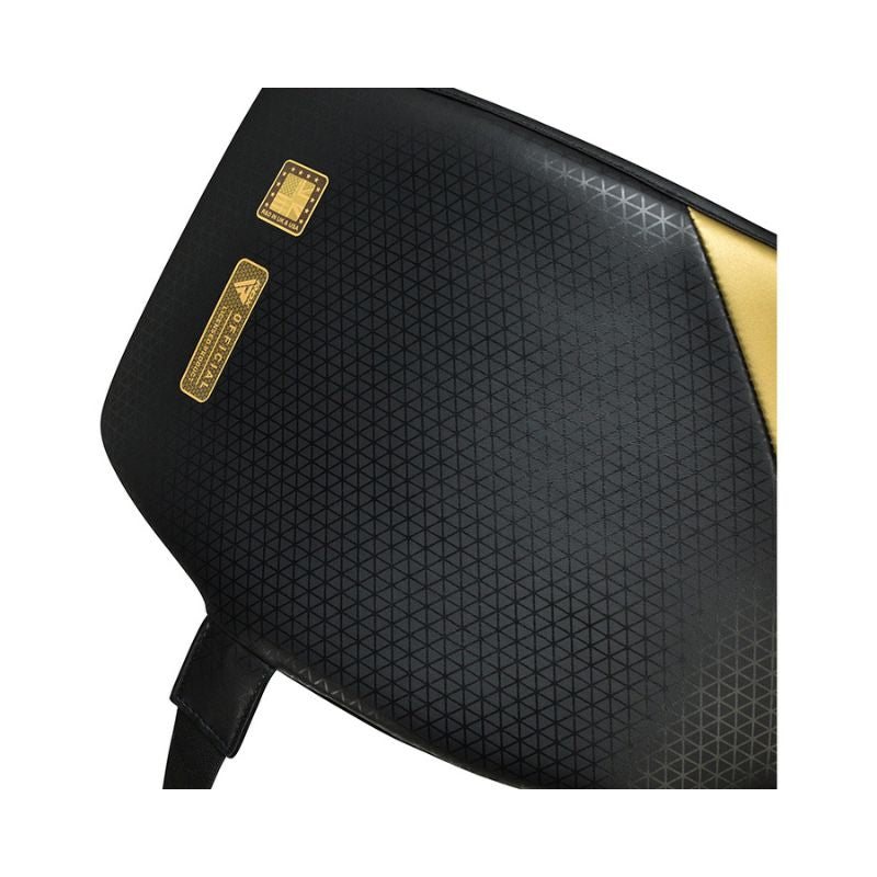 Close-up of a black sports bag with a subtle geometric pattern, gold accents, and a small gold label. A black strap is partially visible at the bottom left.