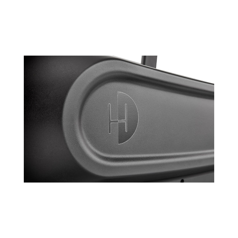 Close-up of a smooth, matte black surface featuring an embossed circular logo with the letter "H" intersected by a vertical line, partially enclosed by a curved line on the right side.
