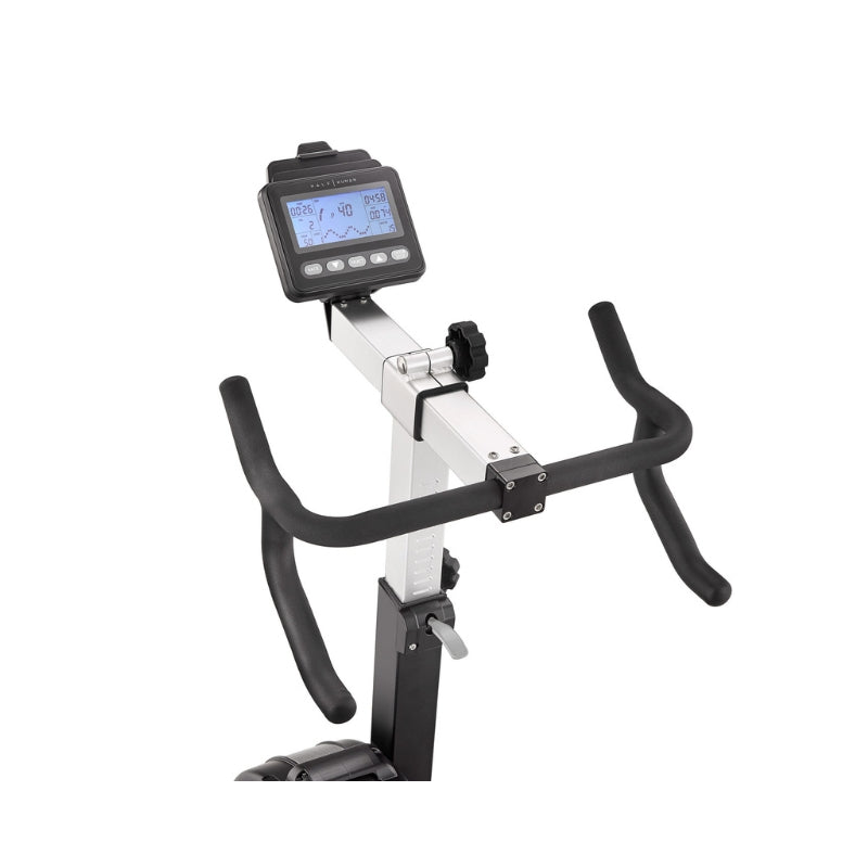 Close-up of a stationary exercise bike’s handlebars and digital display screen, showing workout data such as time, speed, and calories. The bike has a silver and black color scheme against a white background.