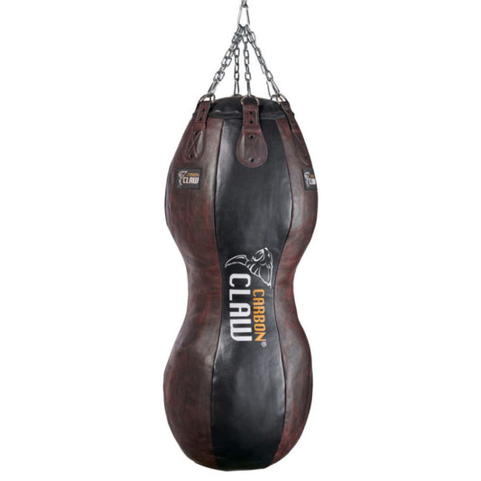 A brown and black hourglass-shaped punch bag from Carbon Claw, the Recoil RB Double Body Heavy Bag (4ft x 18, 65kg, leather), hangs from chains. Its white and yellow logo indicates premium materials, making it ideal for boxing training.