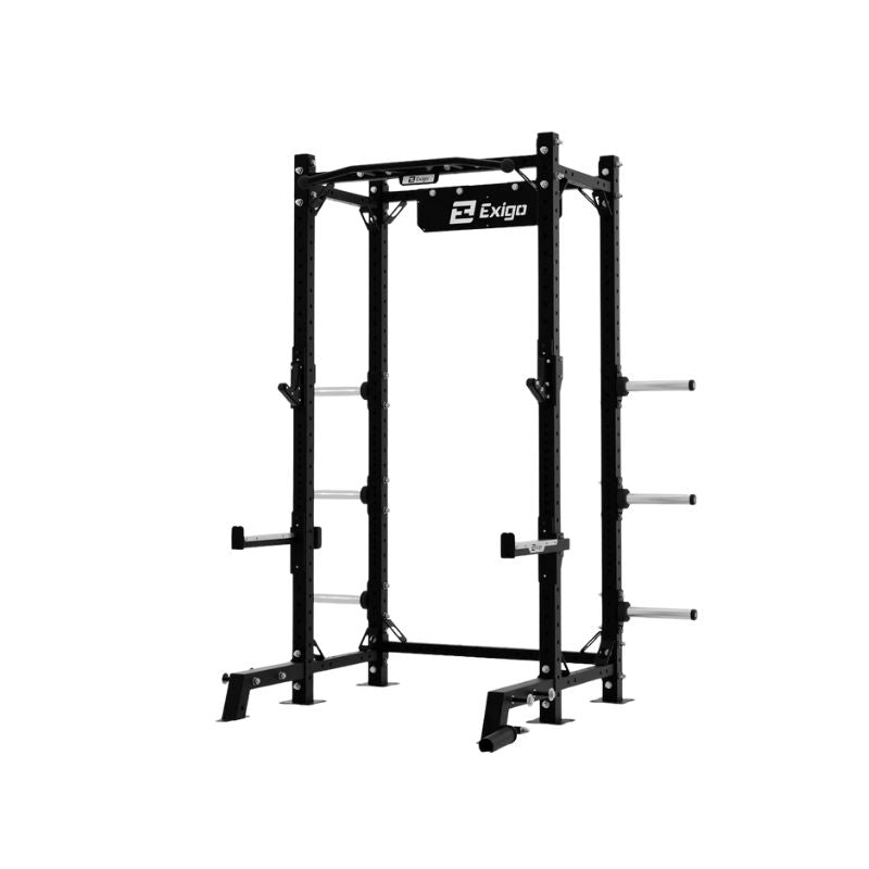 The EXIGO X70 Half Rack by Exigo is a black metal power rack for commercial gyms, featuring safety bars, weight plate storage pegs, and multiple holes for adjustable barbell placement. The Exigo brand name is displayed at the top.