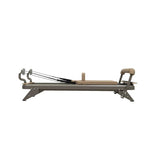 A side view of the Hegren HEGREN TALMA 62 Pilates Reformer—studio-grade steel frame with padded platform, headrest, footbar, and adjustable resistance cords—set against a plain white background. Available for UK delivery.