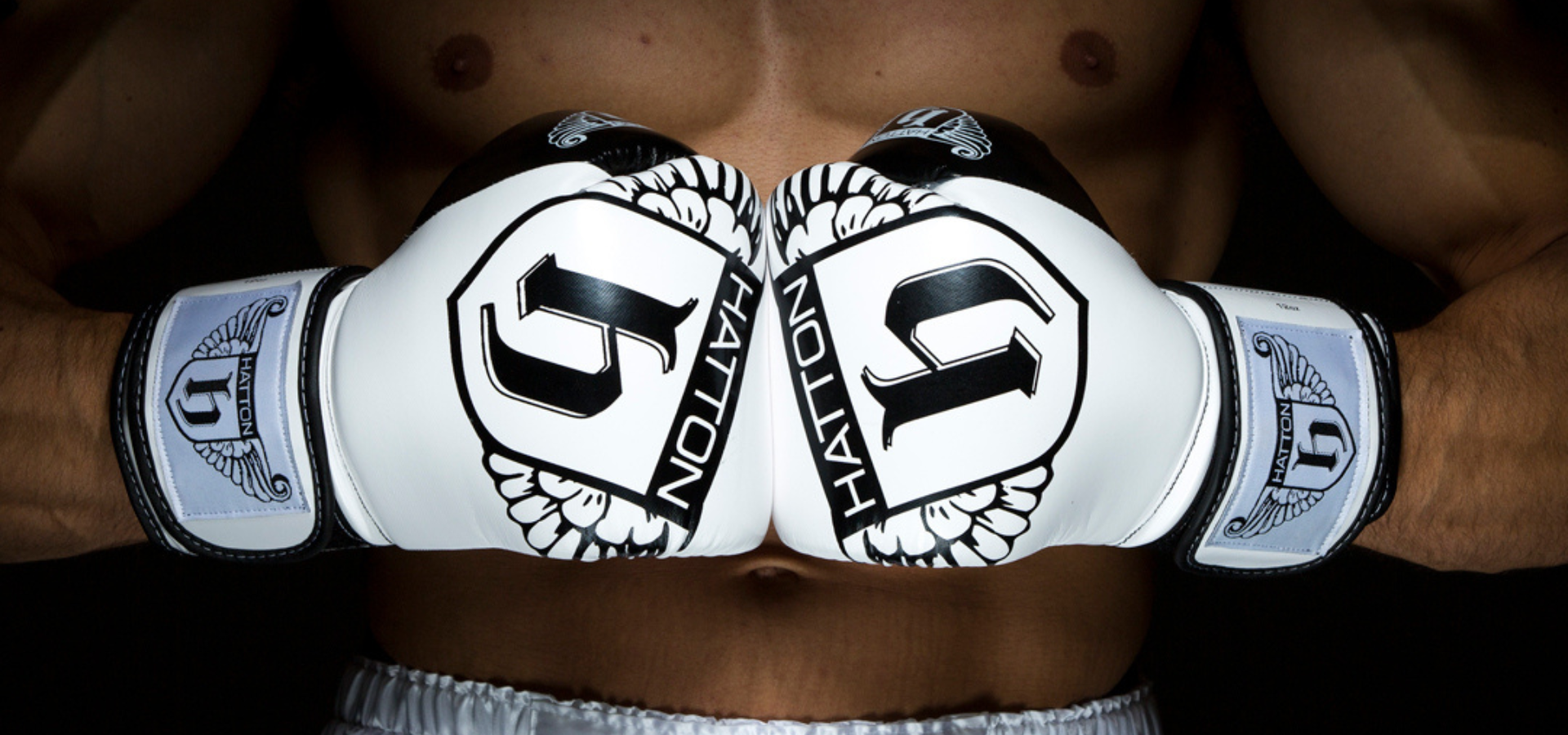 White boxing gloves with black logos held by a person, on a dark background