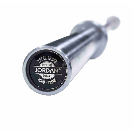 Close-up of the end of a JORDAN Elite Steel High Performance Olympic Bar. The circular cap says JORDAN, 1FT ELITE BAR, ENGLAND, and ESTD 1989 with specs 20KG-28MM. Ideal for Strength Training or Competition, the barbell is horizontally set against a white background.
