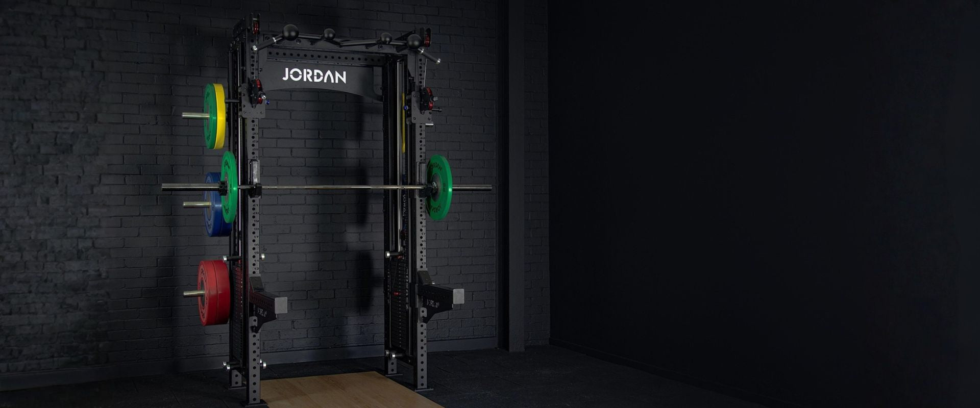 Black weightlifting cage with colorful weight plates on a dark background, featuring the brand 'Jordan'.