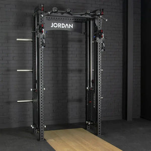 The JORDAN -J75 Cable Rack in black is a versatile gym power rack with barbells and weight plates on both sides. It features storage for weights and equipment, making it ideal for strength training exercises. The top arch is labeled Jordan.
