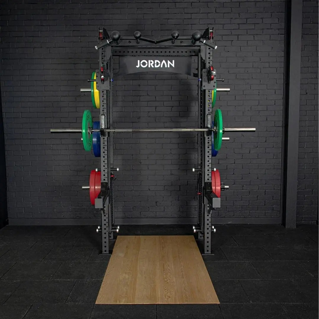The JORDAN -J75 Cable Rack in black is a versatile gym power rack with barbells and weight plates on both sides. It features storage for weights and equipment, making it ideal for strength training exercises. The top arch is labeled Jordan.