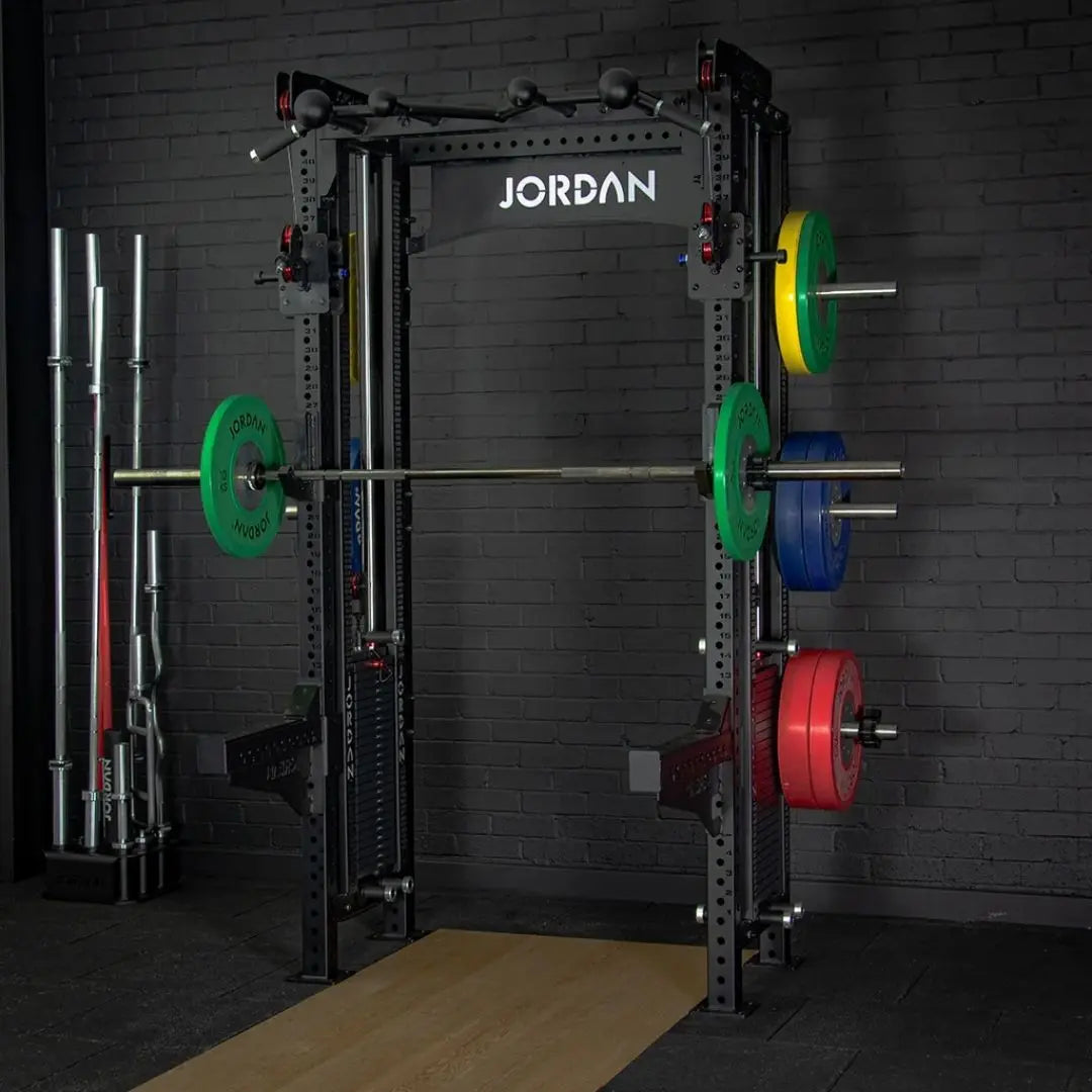The JORDAN -J75 Cable Rack in black is a versatile gym power rack with barbells and weight plates on both sides. It features storage for weights and equipment, making it ideal for strength training exercises. The top arch is labeled Jordan.