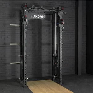 The JORDAN -J75 Cable Rack in black is a versatile gym power rack with barbells and weight plates on both sides. It features storage for weights and equipment, making it ideal for strength training exercises. The top arch is labeled Jordan.