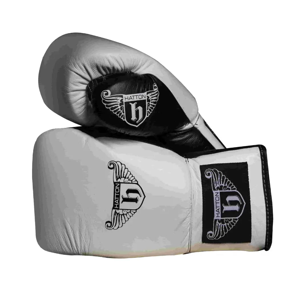The Hatton Boxing Lace Up Gloves from Hatton, crafted in white and black leather, feature intricate shield and wings logo designs on the wrist. These gloves are perfect for sparring, displayed to show both front and thumb sides.